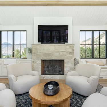 Living room with stone fireplace, white chairs, and a TV above.